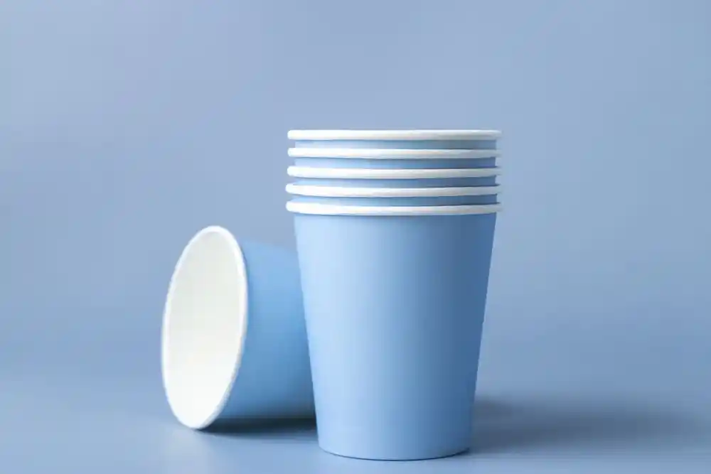 Mavi arka plan önünde üst üste dizilmiş mavi kâğıt bardaklar; bir bardak yan yatmış
