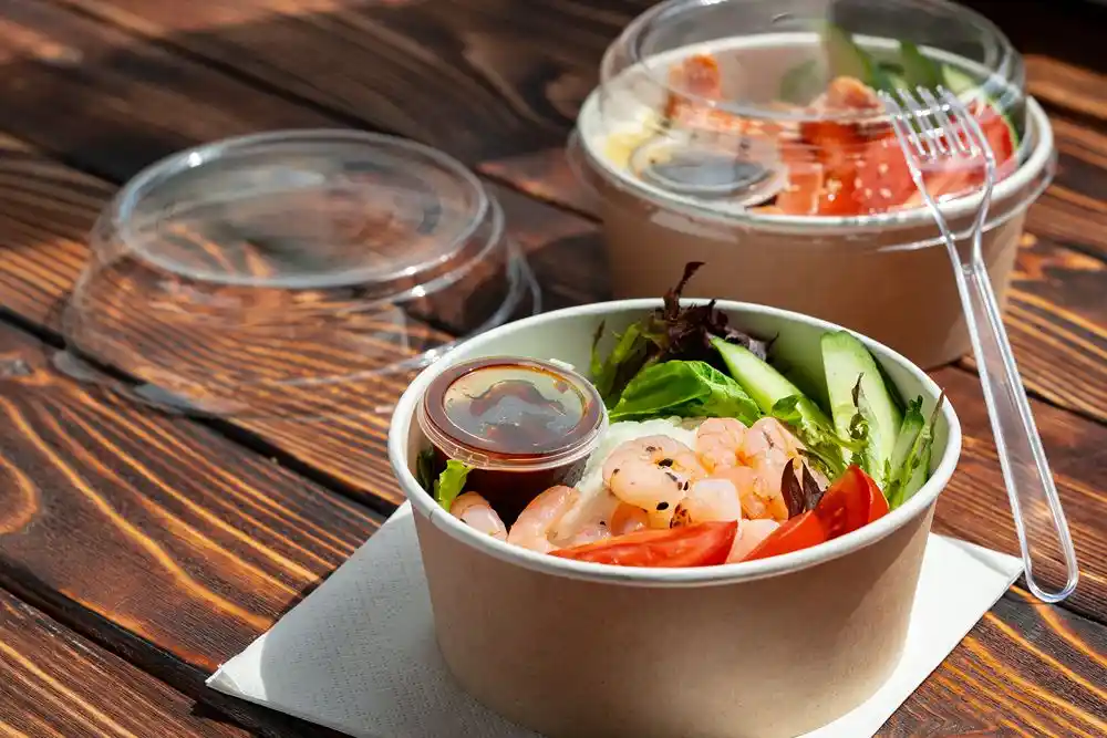 Ahşap masa üzerinde karidesli salata kâsesi ve arka planda domatesli başka bir salata kâsesi